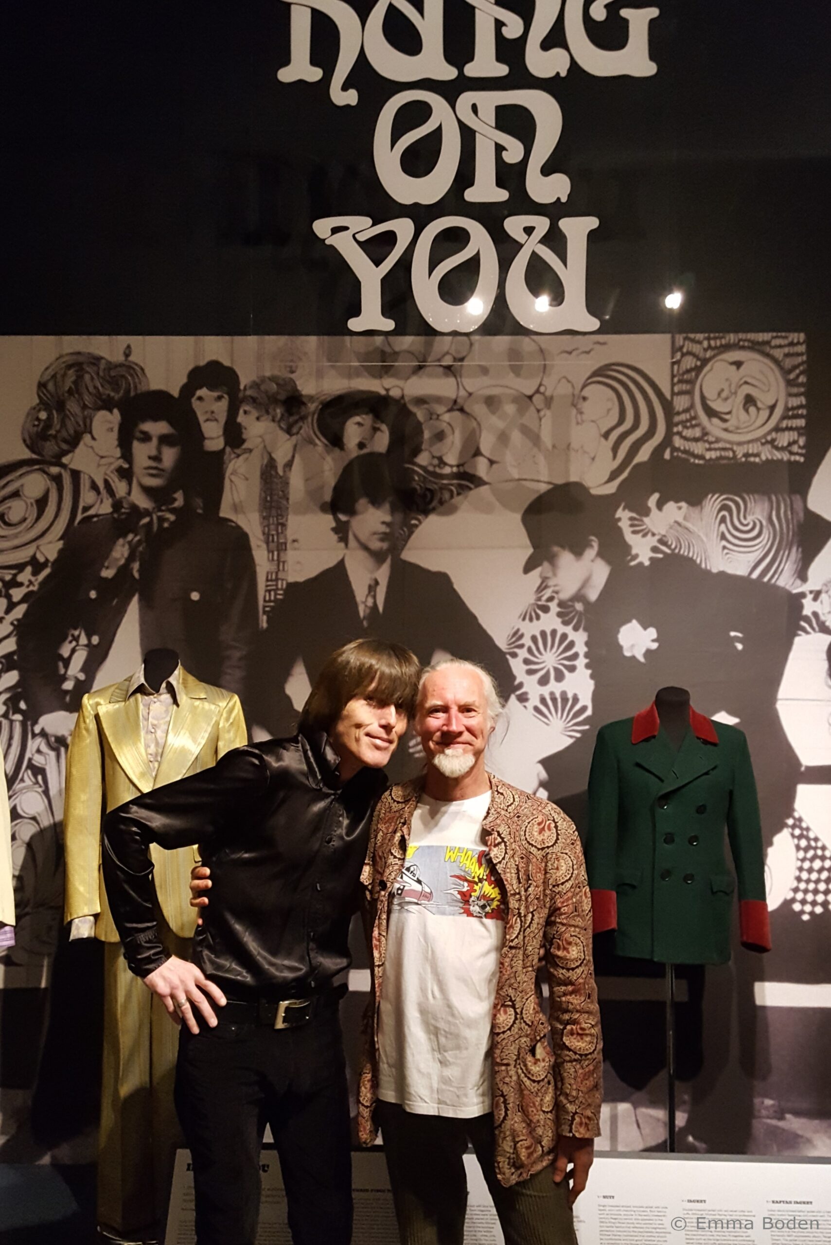 L-R, Peter Feely, collector and lender of men's psychedelic dandy fashion and Mark Butterfield, co-owner and co-curator with wife Cleo of C20 Vintage Fashion, seen standing in front of the Fashion and Textile Museum's Hung On You display, which features an image of the original shop's mural, designed by Anthony Little, who was inspired by Aubrey Beardsley's artworks. Photography by Emma Boden, 2021