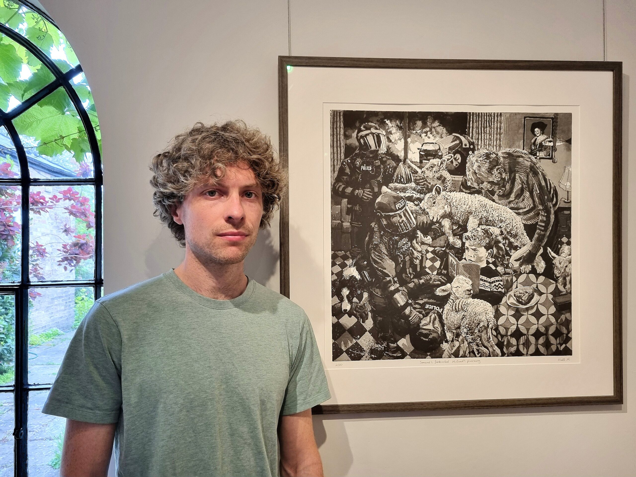 Niall MacCrann next to his award winning etching with aquatint 'Someone's Firebombed McQuaid's Pharmacy' portrait © Emma Boden 2026